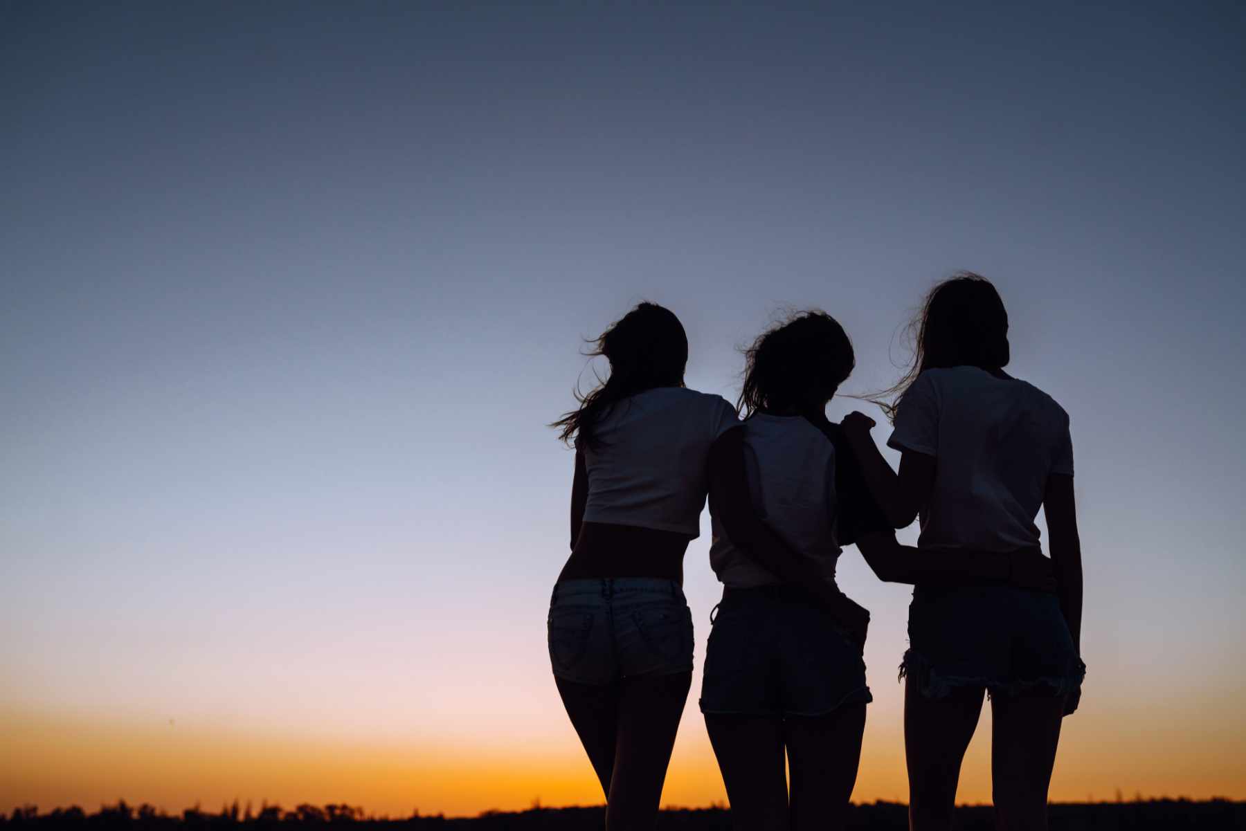 Silhouette of three young girls standing on the beach and looking to a sunset. Summer holidays, vacation